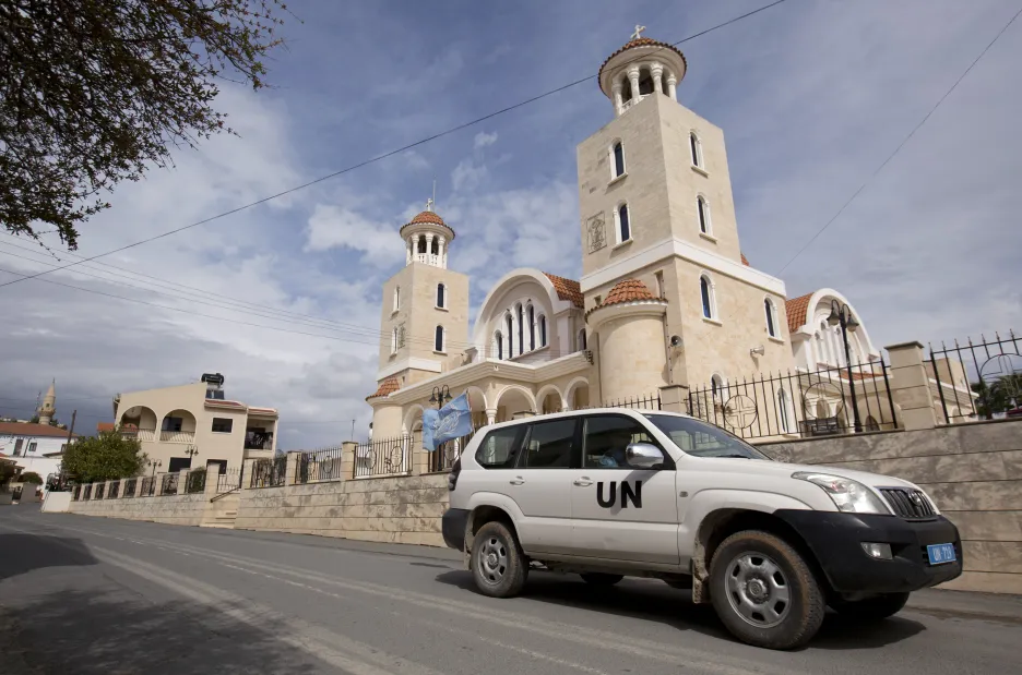 Auto OSN projíždí kolem kostela Agios Georgios, vlevo v pozadí je vidět nedaleká mešita