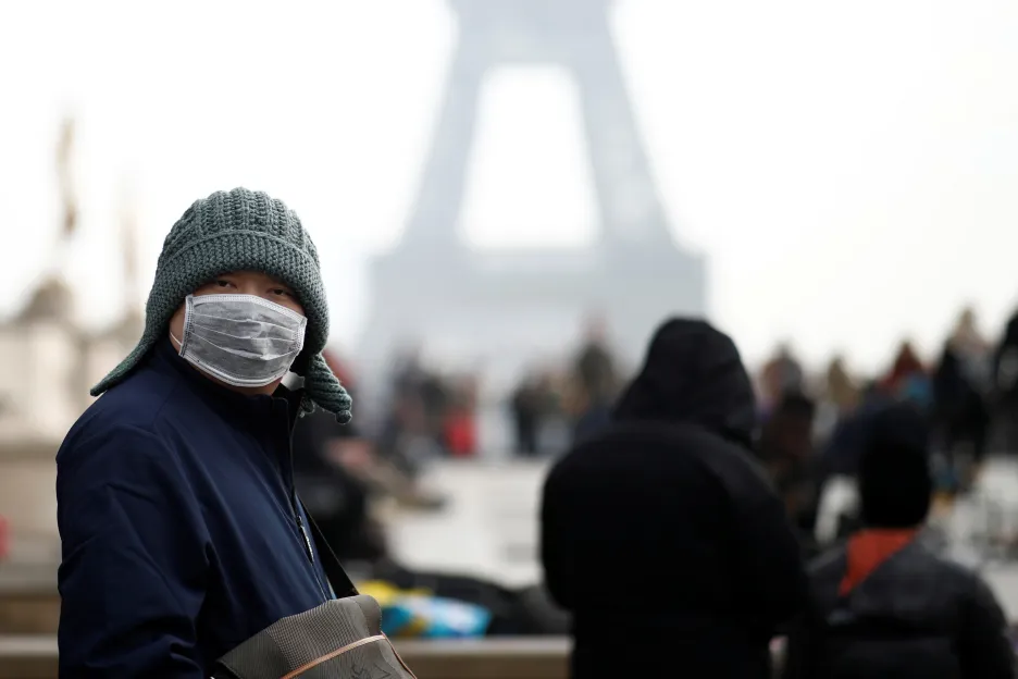 Číňan s maskou před Eiffelovou věží v Paříži