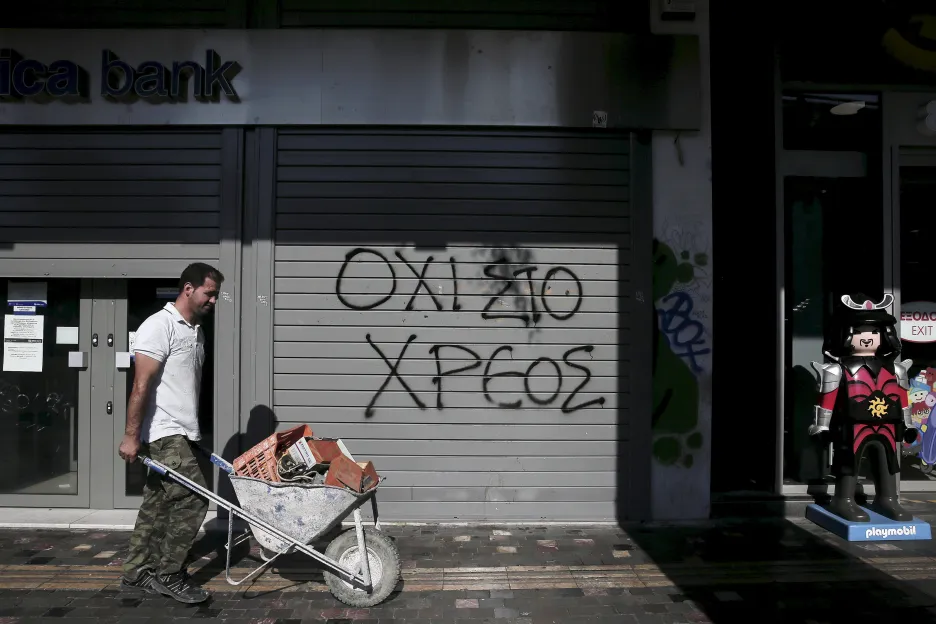 Muž veze kolečko aténskými ulicemi, v pozadí banka s graffiti: 