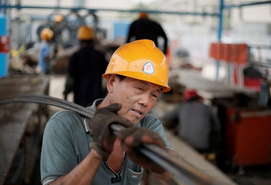 Čínský dělník nese ocelové tyče 