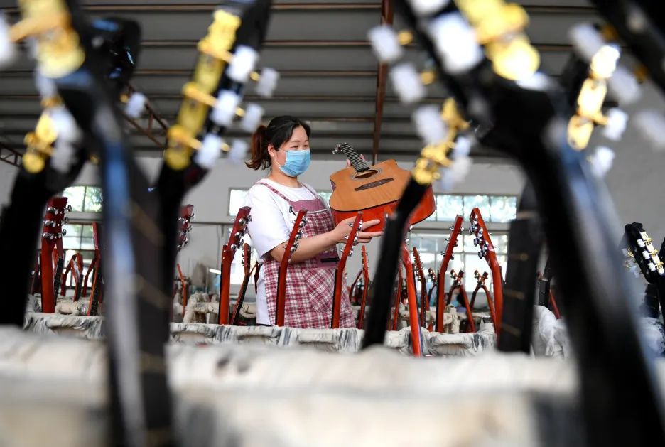 Pracovnice kontroluje kytaru v továrně na hudební nástroje v Číně 