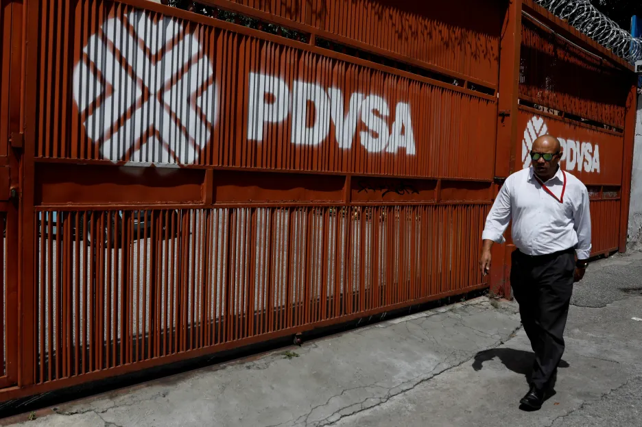 Muž prochází kolem brány s logem venezuelské státní firmy PDVSA