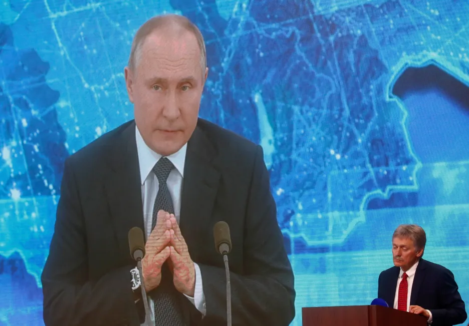 Šéf Kremlu Putin na obrazovce přenosu z tiskové konference, v rohu mluvčí Peskov
