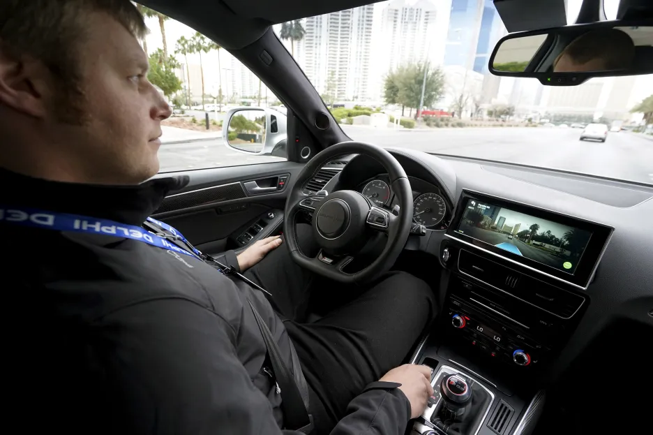 Zástupce firmy Delphi - s rukama mimo volant - ukazuje technologii automatizovaného řízení auta v praxi.