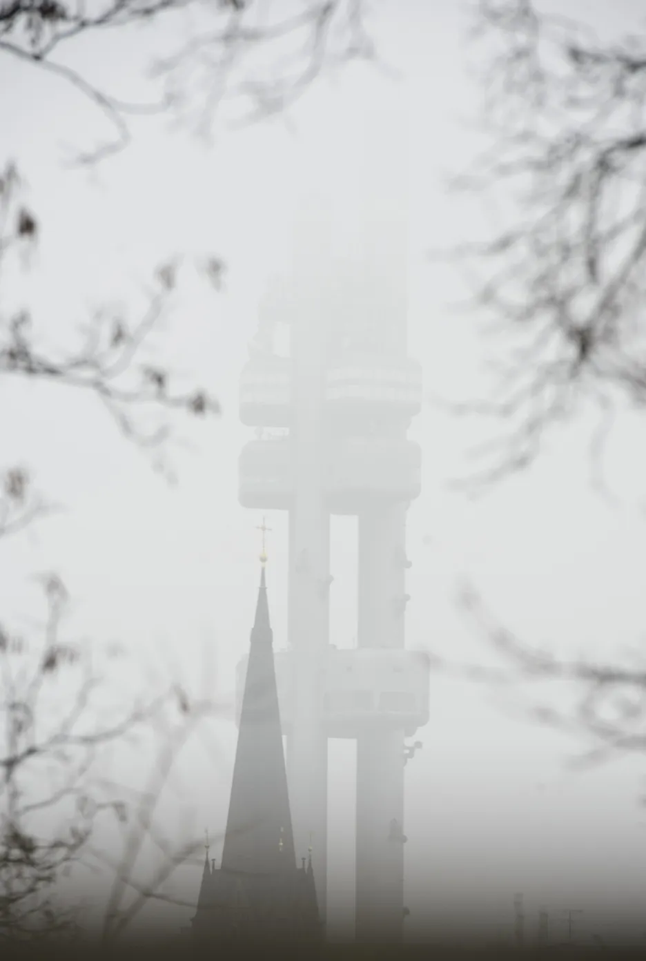 Žižkovský vysílač v mlze, v popředí věž kostela sv. Prokopa