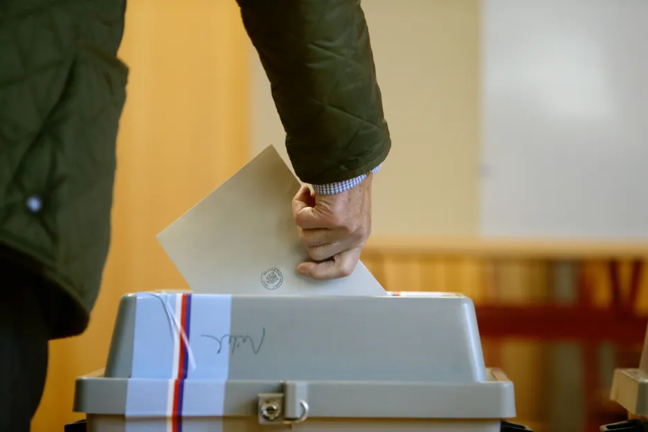 Volič vhazuje obálku do volební urny v Praze.