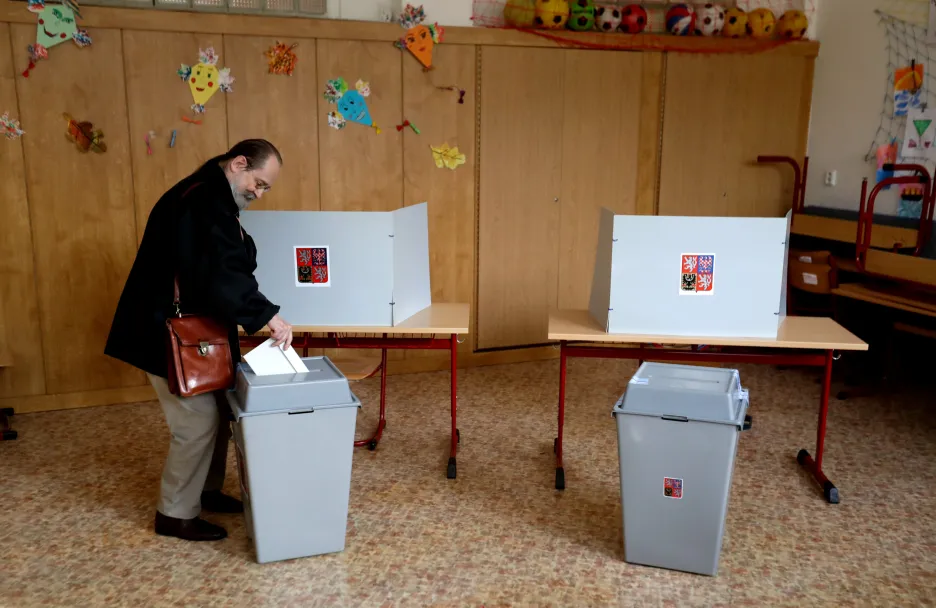 Volič vhazuje obálku do volební urny v Praze.